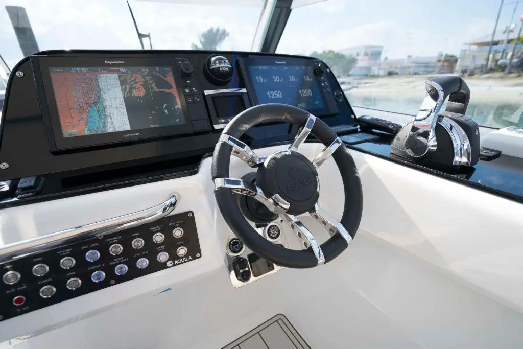 Steering wheel and control panel on a sleek boat, featuring a touchscreen display and navigation controls.
